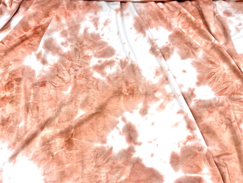May include: A white fabric with a tie-dye pattern in shades of peach and brown.