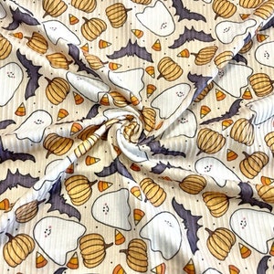 May include: A white fabric with a repeating pattern of orange pumpkins, white ghosts, bats, and candy corn. The fabric has a ribbed texture.