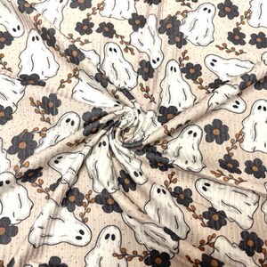 May include: Cream-colored fabric with a repeating pattern of white cartoon ghosts, dark gray flowers, and brown stems. The fabric has a textured, ribbed appearance, suitable for Halloween-themed crafts or apparel.