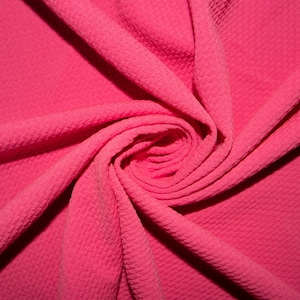 Puede incluir: Primer plano de una tela de color rosa brillante con una textura de tejido de gofre. La tela está doblada y retorcida en forma de espiral.