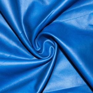 May include: A close-up of a bright blue fabric, arranged in a swirling pattern. The material has a slight sheen, with visible texture and folds creating shadows and highlights. The overall effect is a dynamic display of colour and form.