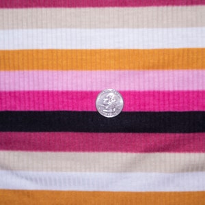May include: A close-up of a striped fabric with alternating bands of pink, white, beige, and orange. A silver coin is resting on the black stripe.