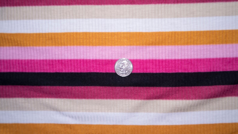 May include: A close-up of a striped fabric with alternating bands of pink, white, beige, and orange. A silver coin is resting on the black stripe.