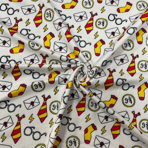 May include: White fabric with a repeating pattern of black-outlined glasses, ties, socks, envelopes, lightning bolts, and "9 3/4" symbols in yellow and red. The fabric is likely for crafting or apparel.