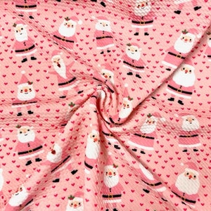 May include: Pink fabric with a repeating pattern of Santa Claus figures and small pink hearts. The Santa Claus figures are wearing red suits with white trim and black boots.