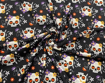 May include: Black fabric with a repeating pattern of white sugar skulls decorated with orange hearts, purple and yellow flowers, and white floral accents. The skulls have a floral crown. The fabric is suitable for Halloween or Day of the Dead projects.