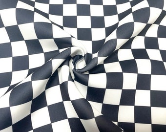 May include: Close-up of a fabric with a black and white checkered pattern. The fabric is draped and folded, creating soft curves and shadows. The classic checkerboard design is a bold and graphic element.