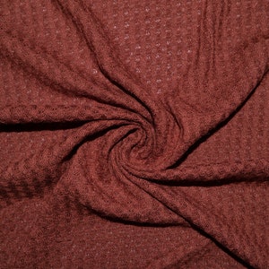 May include: A close-up of a rust-colored waffle knit fabric. The fabric is soft and textured, with a slightly raised waffle pattern.