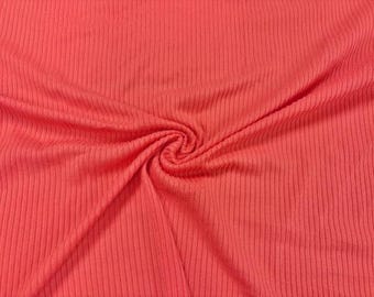 May include: Close-up of a coral-colored ribbed knit fabric. The fabric is folded and swirled, creating a central spiral. The vertical ribbing pattern is visible throughout the material, which appears soft and pliable.
