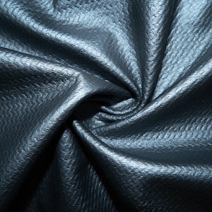 Puede incluir: Primer plano de una tela azul oscuro texturizada con un patrón de espiral. La tela tiene un brillo sutil y una apariencia ligeramente arrugada.