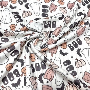 May include: White fabric with a repeating pattern of Halloween-themed illustrations. The design includes ghosts, pumpkins, bats, and the word "BOO" in black. The pumpkins are in shades of peach and brown.