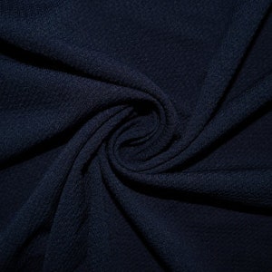 May include: A close-up of a dark blue fabric with a textured surface. The fabric is folded and twisted, creating a swirling pattern.
