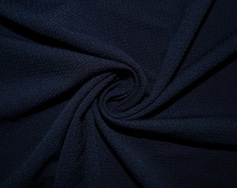 May include: A close-up of a dark blue fabric with a textured surface. The fabric is folded and twisted, creating a swirling pattern.