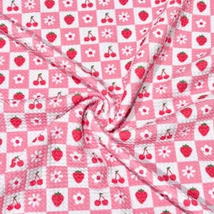 May include: Pink and white checkered fabric with a repeating pattern of red strawberries, cherries, and white flowers. The fabric is textured and has a slight sheen, with a swirled appearance.