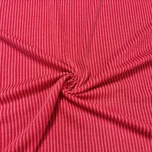 May include: Close-up of a vibrant red fabric with a textured, ribbed design. The material is folded and twisted, showcasing vertical stripes in varying shades of red. The fabric appears soft and pliable.