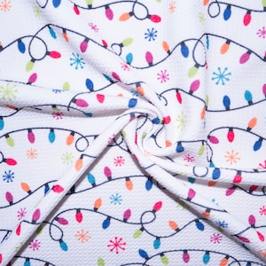 May include: A white fabric featuring a repeating pattern of black string lights with colorful bulbs in red, blue, green, and orange, interspersed with small, multi-colored star-shaped snowflake icons across the textured material surface.