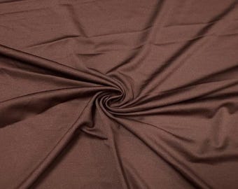 Könnte beinhalten: Nahaufnahme eines Wirbels aus braunem Stoff. Das Material ist drapiert und gefaltet, wodurch ein strukturiertes Muster entsteht. Der Stoff scheint weich und fließend zu sein, mit subtilen Glanzlichtern und Schatten.