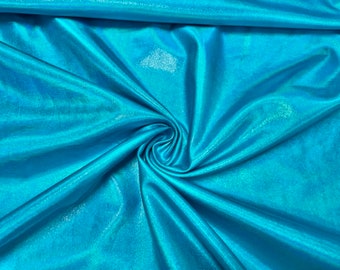 May include: A close-up of a turquoise iridescent fabric with a smooth, silky texture. The fabric is folded and draped, showcasing its sheen and shimmer.