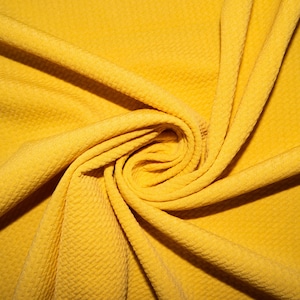 Puede incluir: Primer plano de una tela amarilla con superficie texturizada. La tela está doblada y retorcida en forma de espiral.