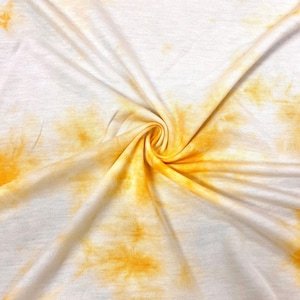 May include: White fabric with a yellow tie-dye pattern. The fabric is bunched up in the center, creating a swirl effect.