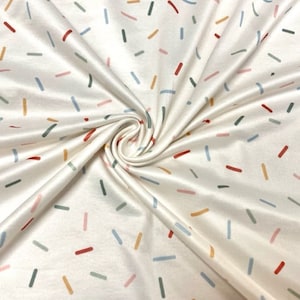 Könnte beinhalten: Weißer Stoff mit einem verstreuten Muster aus bunten Linien. Die Linien sind in Rot-, Orange-, Blau-, Grün- und Rosatönen.