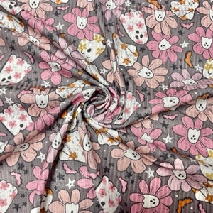 May include: A gray fabric with a repeating pattern of pink and peach flowers, ghost-like figures, and small stars. The flowers have white centers and the ghosts have floral patterns. The fabric is slightly textured.