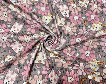 May include: Grey fabric featuring a repeating pattern of pink and peach flowers, ghost-like figures, and small stars. The flowers have white centres and the ghosts have floral patterns. The fabric has a textured appearance.
