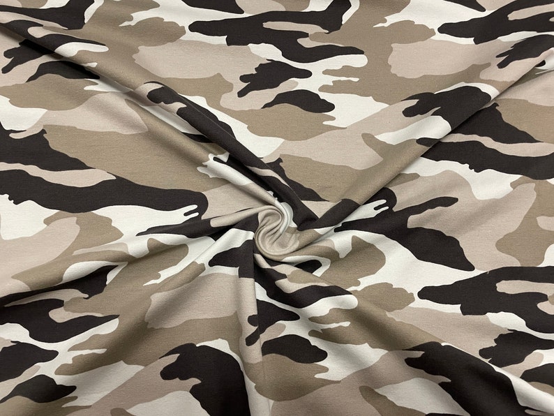 May include: A close-up of a beige, brown, and black camouflage fabric. The fabric is folded and has a soft, textured feel.