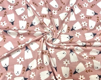 May include: Pink fabric featuring a repeating pattern of white ghosts in black witch hats, white daisies, and brown leaves. The fabric is folded, creating shadows and texture. Suitable for Halloween or spooky crafts.