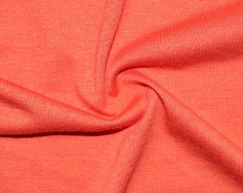 Puede incluir: Primer plano de una tela de color coral con una superficie suave y texturizada. La tela está doblada y drapeada, mostrando su textura suave y fluida.