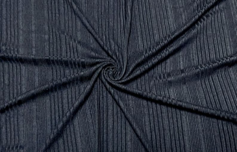 May include: Dark navy blue fabric with a ribbed texture. The fabric is gathered in a spiral pattern, creating a swirl effect. The vertical ribs give the fabric a textured appearance. The fabric appears to be soft and flexible.