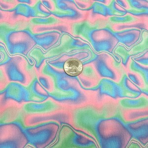 May include: Close-up of a fabric with a wavy, abstract pattern in pastel colours. The design features flowing lines of pink, green, and blue. A U.S. quarter coin is placed on the fabric for scale.
