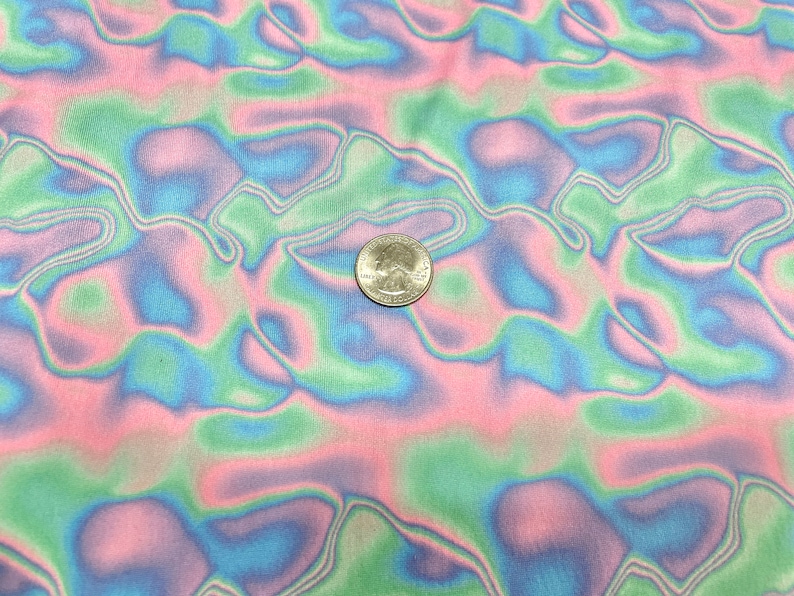 May include: Close-up of a fabric with a wavy, abstract pattern in pastel colours. The design features flowing lines of pink, green, and blue. A U.S. quarter coin is placed on the fabric for scale.