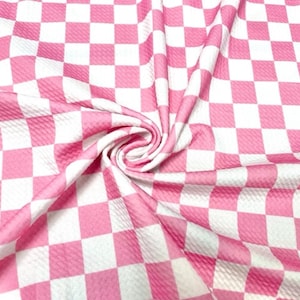 May include: A close-up of a fabric with a pink and white checkered pattern. The fabric is soft and has a slight texture. The squares are evenly sized and create a visually appealing design. The fabric is folded and draped.