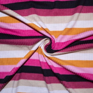 May include: Close-up of a striped fabric with alternating bands of pink, white, beige, orange, and black. The fabric is folded and twisted, creating a swirling pattern.