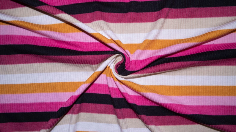 May include: Close-up of a striped fabric with alternating bands of pink, white, beige, orange, and black. The fabric is folded and twisted, creating a swirling pattern.