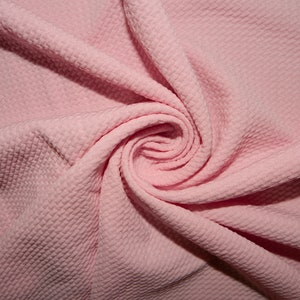 Puede incluir: Primer plano de una tela texturizada rosa con un patrón de gofrado. La tela está doblada y retorcida, creando una forma espiral.