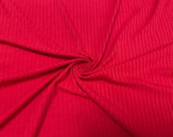 May include: Red ribbed fabric with a textured surface. The fabric is folded and draped, showing the texture and the color.