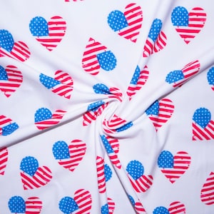 May include: White fabric with a repeating pattern of hearts featuring the American flag design. The hearts have red and white stripes and a blue field with white stars. The fabric is folded and draped.