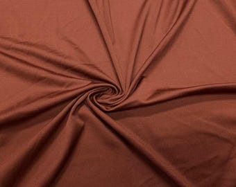 Könnte beinhalten: Nahaufnahme eines gewirbelten, rostfarbenen Stoffes. Das Material ist glatt und drapiert sich in weichen Falten, mit einer zentralen Spirale. Der Stoff hat einen leichten Glanz, der auf eine Satin- oder ähnliche Webart hindeutet. Der Gesamteindruck ist reich und luxuriös.