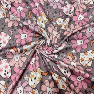 May include: A fabric with a repeating pattern of pink and peach flowers, white ghosts, bats, and stars on a gray background. The flowers have a daisy-like appearance, and the ghosts have smiling faces. The overall theme is a Halloween or spooky floral design.