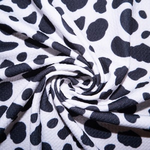 May include: White fabric with a black dalmatian spot pattern. The fabric is tightly woven and has a slight texture. The fabric is folded and draped, showing the pattern's repeating design. The fabric is suitable for clothing or home decor.