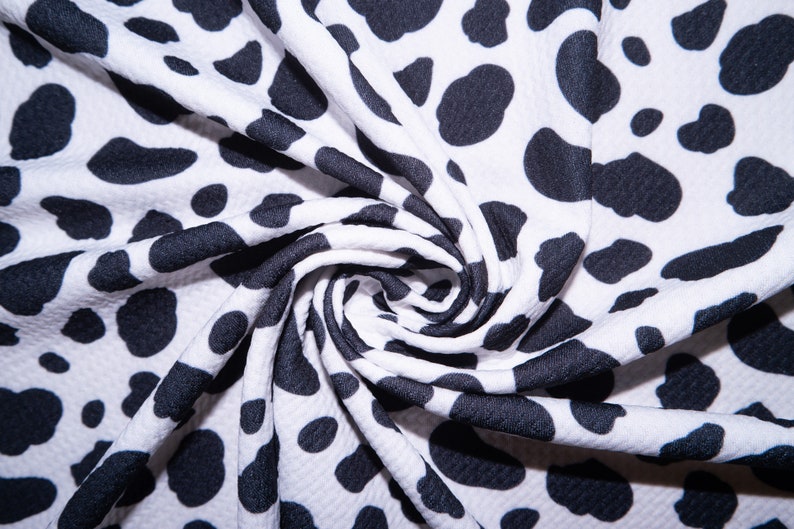 May include: White fabric with a black dalmatian spot pattern. The fabric is tightly woven and has a slight texture. The fabric is folded and draped, showing the pattern's repeating design. The fabric is suitable for clothing or home decor.