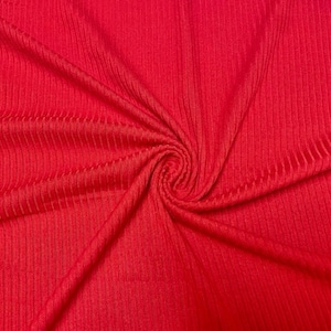 May include: Red ribbed fabric with a textured surface. The fabric is folded and draped, showing the texture and drape of the material.