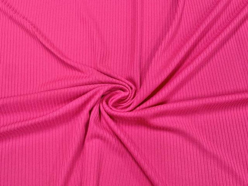 Op de afbeelding: Felroze geribbelde gebreide stof met verticale lijnen. De stof is in een spiraal verzameld, waardoor een textuurpatroon ontstaat. Het materiaal heeft een zachte, vloeiende uitstraling, ideaal voor kleding of woondecoratieprojecten.