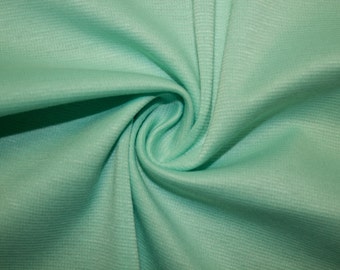 Peut inclure: Gros plan sur un tissu doux de couleur vert clair avec une texture légèrement côtelée. Le tissu est plié et drapé, mettant en valeur sa douceur et sa flexibilité.