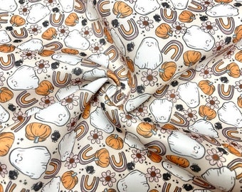 May include: A cream-coloured fabric with a repeating pattern of white ghosts, orange pumpkins, rainbows, and flowers. The fabric has a subtle texture.