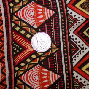 May include: Close-up of a fabric with a vibrant geometric pattern. The design features repeating shapes in red, orange, yellow, and black, with a quarter coin for scale. The fabric has a tribal or ethnic aesthetic.
