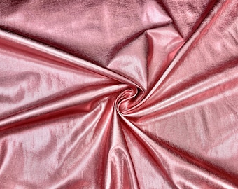 May include: A close-up of a shiny, rose-gold fabric with a textured surface. The fabric is gathered in a swirl, creating folds and shadows that highlight its metallic sheen. This material is suitable for apparel and craft projects.