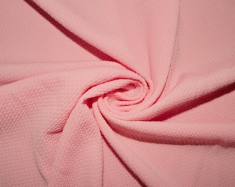 May include: A close-up of a soft, pink fabric with a textured waffle-like pattern. The fabric is folded and twisted, creating a swirling effect.